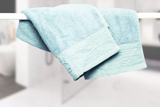 Hanging Towels. Close-up of a blue soft terry bath towel hanging on a clothes rail against a blurred light blue bath background.