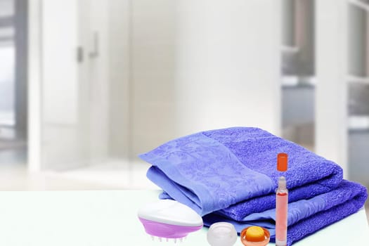 Table top on towels background. Closeup of fresh soft terry bath towels with massage brush, cosmetic cream and soap bottle over blurred bathroom background. Space.