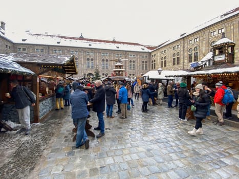 Munich, DE, Dec. 19 2022  People exploring the festive Christmas market in the snowy courtyard of the Munich Residenz, surrounded by decorated stalls and holiday lights