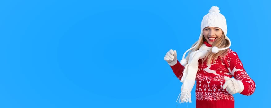 Young woman in red winter pullover jumper, white gloves, ski hat and muffetee, smilling happily, isolated on blue background (replace with your image or add text to copy space)
