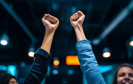 Two raised fists against illuminated background expressing triumph and unity at event venue, dramatic lighting creates powerful atmosphere.