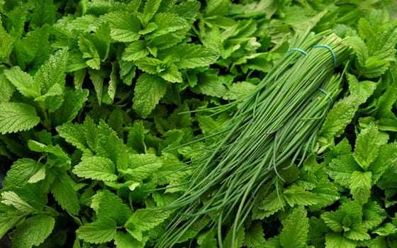 Bunch of chives over bright green mint leaves displayed on herbs market