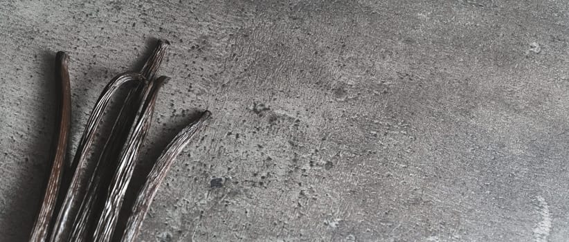 Bourbon vanilla beans on dark gray working board, view from above, wide banner with space for text right side