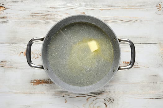 Overhead view of a piece of butter melts in a pan on a wooden table