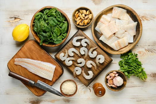 Top view of fresh ingredients including shrimp, fish, spinach, lemon, and mussels arranged on wooden boards