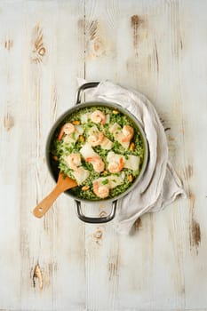 Green rice risotto with white fish, mussels and shrimps in a rustic casserole on wooden kitchen tabletop, evoking a warm, home-cooked meal atmosphere.