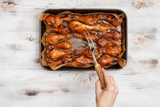 A hand holds a fork to serve crispy baked chicken drumsticks arranged on a tray. The setup is on a rustic wooden table, creating a cozy dining atmosphere perfect for a family meal.