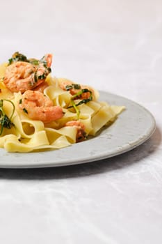 A serving of shrimp fettuccine garnished with fresh herbs is elegantly presented on a gray plate, showcasing a delightful blend of flavors and colors, perfect for a special meal or family dinner.