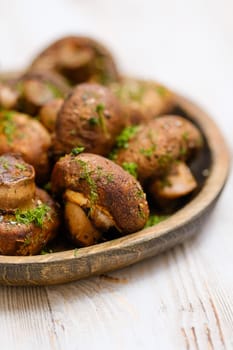 Close-up view of a wooden platter with freshly cooked champignon mushrooms, lightly seasoned with herbs. The dish is set against a rustic background, showcasing vibrant colors and textures.