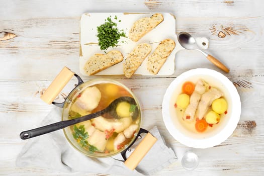 A hearty fish soup in a pot, filled with fish fillet, vegetables and herbs. Slices of seasoned bread accompany the warm bowl, ready for a comforting meal on a cool day.