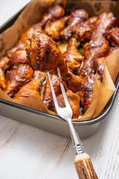 A fork lifts a perfectly cooked chicken drumstick from a baking tray with parchment paper. The succulent pieces are glazed to a rich brown, showcasing an appetizing grilled appearance.