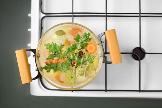 A pot of simmering vegetable broth filled with assorted fresh carrots, potatoes, herbs, and spices rests on a stovetop. The vibrant colors and aromas create a warm, inviting atmosphere for cooking.