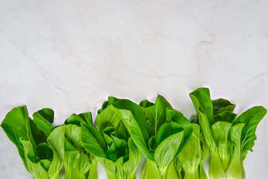 A vibrant display of fresh bok choy sits neatly aligned on a marble countertop. The greens shine under natural light, showcasing their crisp texture and healthy appearance, perfect for cooking.
