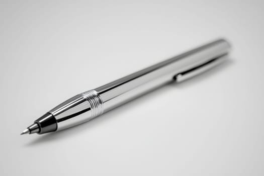A sleek silver pen lies on a smooth light gray surface, showcasing its shiny metallic finish. The simplicity of the setting emphasizes the pens design and craftsmanship.