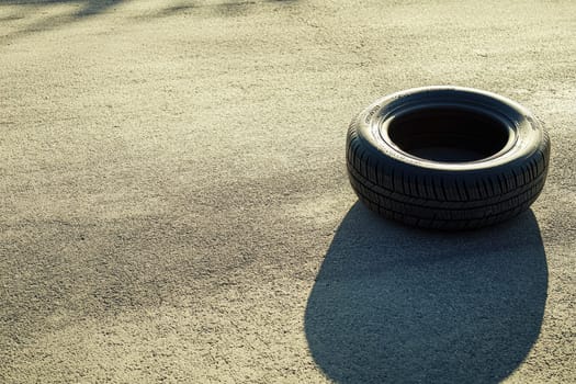 Captured from above, this image showcases a single summer tire resting on a sunlit pavement. The smooth texture of the asphalt contrasts with the tire's round shape, creating a simple yet striking visual.