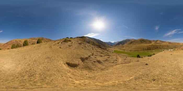 Full Spherical panorama of dry dust covered hill in mountains with blue sky and sun above at autumn day in equirectangular projection