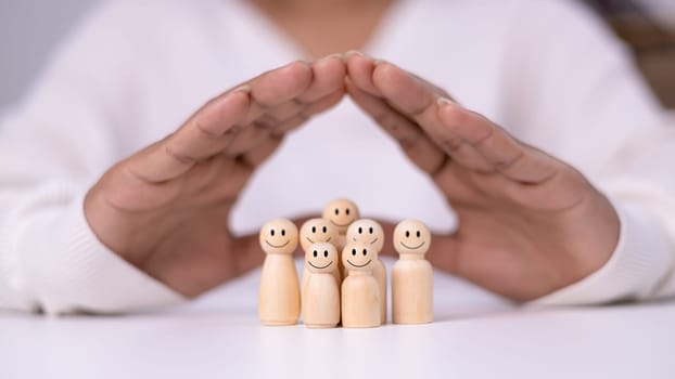 Hand of a person laying down protection a wooden dolls to show represents the protection of family safety, Insurance management planning, Health care and finance, Property and family risk reduction.
