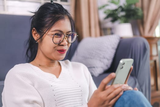 Selective focus, Happy young woman sitting on sofa enjoy using mobile phone for online shopping cashless in living room at home, Holding smartphone, reading good news in unexpected message or email.