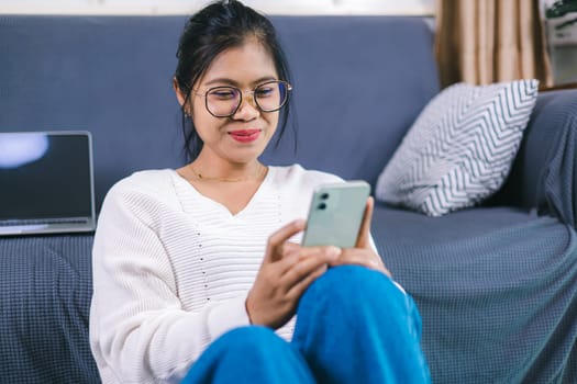 Selective focus, Happy young woman sitting on sofa enjoy using mobile phone for online shopping cashless in living room at home, Holding smartphone, reading good news in unexpected message or email.