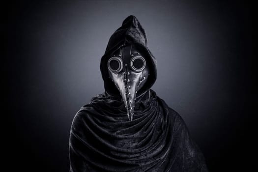 Plague doctor in hooded cloak at night over dark misty background