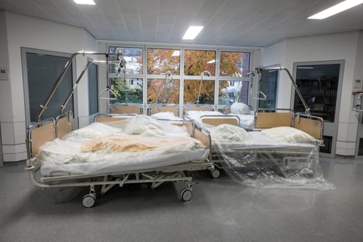 leere Krankenhausbetten stehen mit Folie abgedeckt in einem Krankenhausflur - Symbolbild