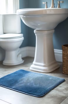 A clean bathroom featuring a blue rug, white toilet, and elegant sink. The soft colors create a calming atmosphere.