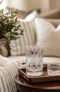 Elegant glassware sits on a wooden tray amidst a welcoming living room, featuring stylish cushions and a decorative floral arrangement.