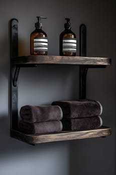 A wooden shelf mounted on a dark wall displays neatly stacked towels and elegant bottles, creating a modern bathroom ambiance.
