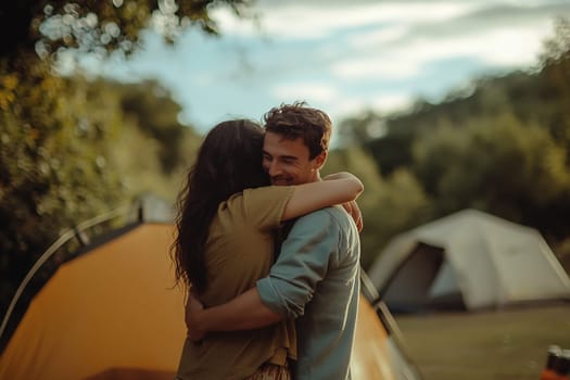 A joyful couple shares a warm embrace in nature, surrounded by camping tents and a serene landscape during golden hour.