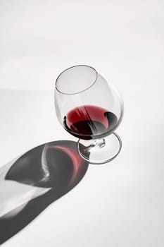 A glass filled with deep red wine casts an intriguing shadow on a light surface, showcasing its vibrant color and curvature.