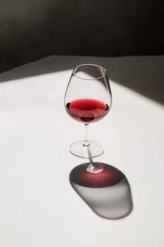 A wine glass filled with red wine sits on a white surface, illuminated by soft light that creates a delicate shadow.