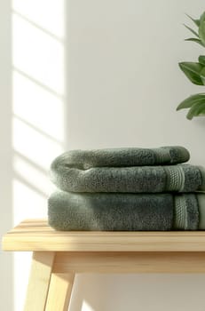 Soft green towels are neatly folded on a wooden shelf, illuminated by warm sunlight filtering through nearby window blinds.