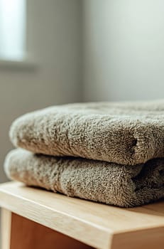 Two plush, well-folded towels sit on a wooden table in a cozy, softly lit room, offering comfort and relaxation.