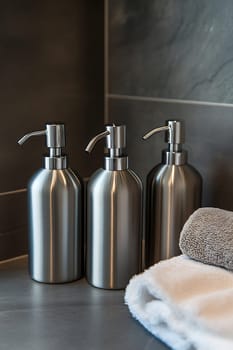 Three sleek metal dispensers stand together on a bathroom counter beside a soft gray towel, enhancing the modern decor of the space.