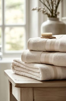 Plush towels are stacked neatly on a wooden table with a comb and a vase in the background, creating a serene bathroom ambiance.