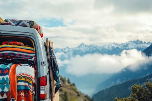 A van with colorful blankets is parked on a mountain overlook, showcasing a stunning landscape of peaks and clouds in the distance.