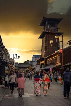 tokyo, japan - dec 31 2022: Tourists in kimono strolling at dusk in Kashiya or Dagashi Yokochô street of Koedo Kawagoe historic district with its landmark Time Bell Tower builded in Kurazukuri style.
