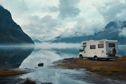 A camper van parked lakeside surrounded by majestic mountains and misty clouds during early morning light.
