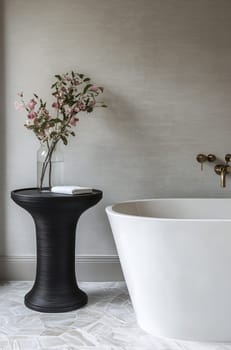 A stylish bathroom featuring a sleek white bathtub, a unique black side table, and delicate flowers in a vase, creating a serene atmosphere.