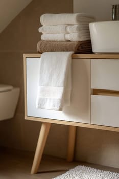 Soft towels are stacked alongside a clean sink in a contemporary bathroom, showcasing minimalistic design and a warm atmosphere.