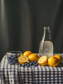 A glass bottle filled with lemonade sits on a checkered cloth, surrounded by fresh lemons and blueberries, creating a refreshing setting.