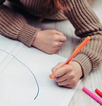 Young child, lying on their stomach, is engrossed in drawing curves on a sheet of graph paper using colorful markers, indicating a focus on learning and creativity