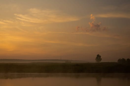 Lake at sunset, coastal grass and trees. The light of the sunset above the water.