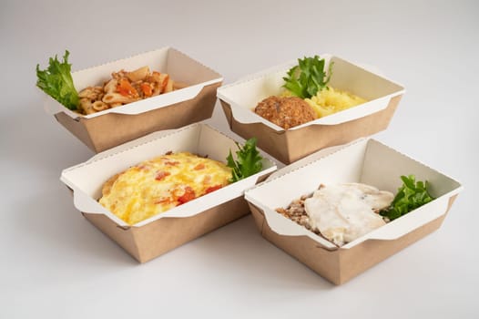 Four takeout meals served in biodegradable containers, featuring pasta, casserole, mashed potatoes with meatball, and buckwheat with chicken, garnished with greens.
