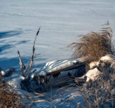 Broken wooden pier by the river in winter in the snow.