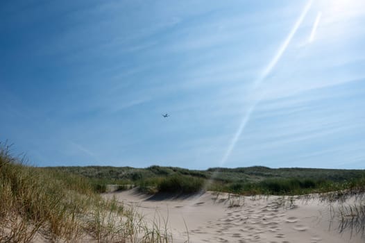 Dune  with beach grass, sun and an airplane on the North Sea coast in the Netherlands