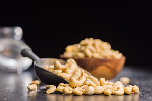 Roasted cashew nuts in scoop on a black table.