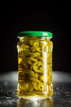 Pickled sliced jalapeno peppers in jar on a black table.