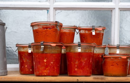 A row of glass jars filled with red sauce. The jars are stacked on top of each other, creating a sense of abundance and variety. The scene conveys a feeling of warmth and comfort