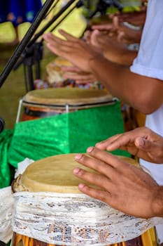 Hands playing several atabaque drums decorated with fabric being used during an Umbanda religious ceremony in Brazil